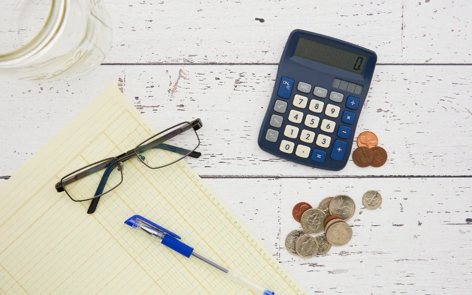 Calculator, coins and a notepad on a desk